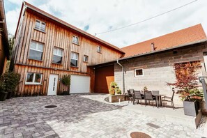 A two-story wooden building with a garage, a paved courtyard, and outdoor seating.