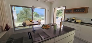 A modern kitchen with a large island, a dining area with a view, and a coffee station. - Eliá Luxury Villa with a Jacuzzi and Privacy, in the Heart of Crete (Kalonichti)