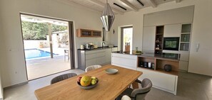 A modern kitchen with a dining area, a pool visible through the glass door, and a pendant light. - Eliá Luxury Villa with a Jacuzzi and Privacy, in the Heart of Crete (Kalonichti)