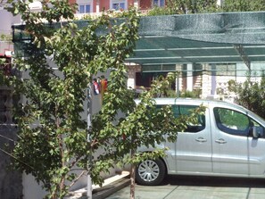 Ein silbernes Auto vor einem Gebäude mit einer grünen Markise und einem Baum mit grünen Blättern.