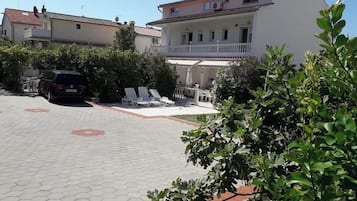A residential building with a paved driveway, a car parked in the driveway, and a balcony with outdoor furniture.
