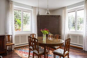 A dining room with a round table, six chairs, a vase with flowers, and large windows with curtains. - Aventino Luxury Amazing Apartment (Roma)