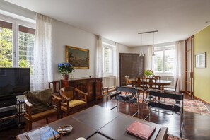 Een woonkamer met een televisie, houten meubels, een eettafel en een groot raam met gordijnen.