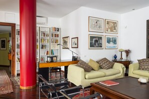 Een woonkamer met een rode kolom, een beige bank, een salontafel en een boekenplank vol boeken.