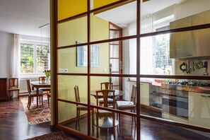 A dining area with a table and chairs, a kitchen with appliances, and a view through a glass partition. - Aventino Luxury Amazing Apartment (Roma)