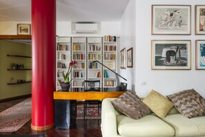 A living room with a red pillar, a bookshelf, a sofa with patterned cushions, and framed artwork on the wall. - Aventino Luxury Amazing Apartment (Roma)