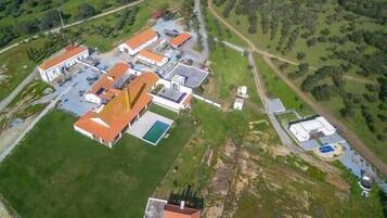 An aerial view of a property with multiple buildings, including a main building with a red roof, a swimming pool, and a smaller structure with a blue roof.