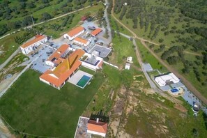 Ett flygbildsbild av en fastighet med flera byggnader, inklusive en huvudbyggnad med ett rött tak, en swimmingpool och en mindre byggnad med ett blått tak.