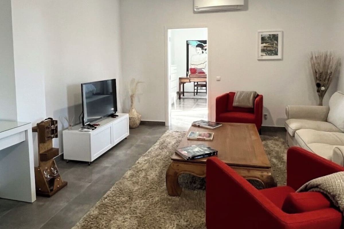 Un salon moderne avec un téléviseur à écran plat posé sur un meuble blanc, une table basse en bois, des canapés rouges et beiges, et un tapis beige.