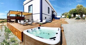 Ett modernt hus med en träaltan, ett bubbelbad och en täckt uteplats.