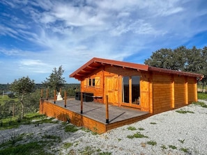 A wooden cabin with a deck, large windows, and a view of the landscape.