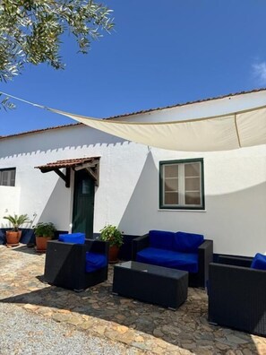 A patio with outdoor furniture, a white building, and a large shade sail.