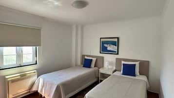 A hotel room with two beds, a window, a radiator, and a rug.