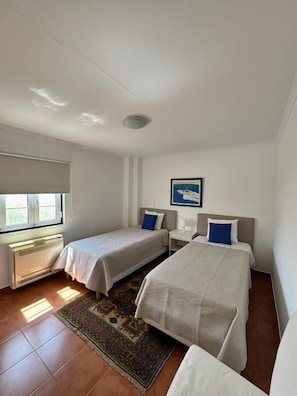 A hotel room with two beds, a window, a radiator, and a rug.