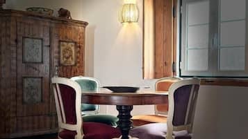 A dining area with a round table, four chairs, a wooden cabinet with pictures, and a window with frosted glass.