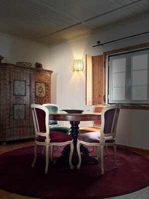 Un coin repas comprenant une table ronde, quatre chaises, un meuble en bois orné de tableaux et une fenêtre à vitrage dépoli.
