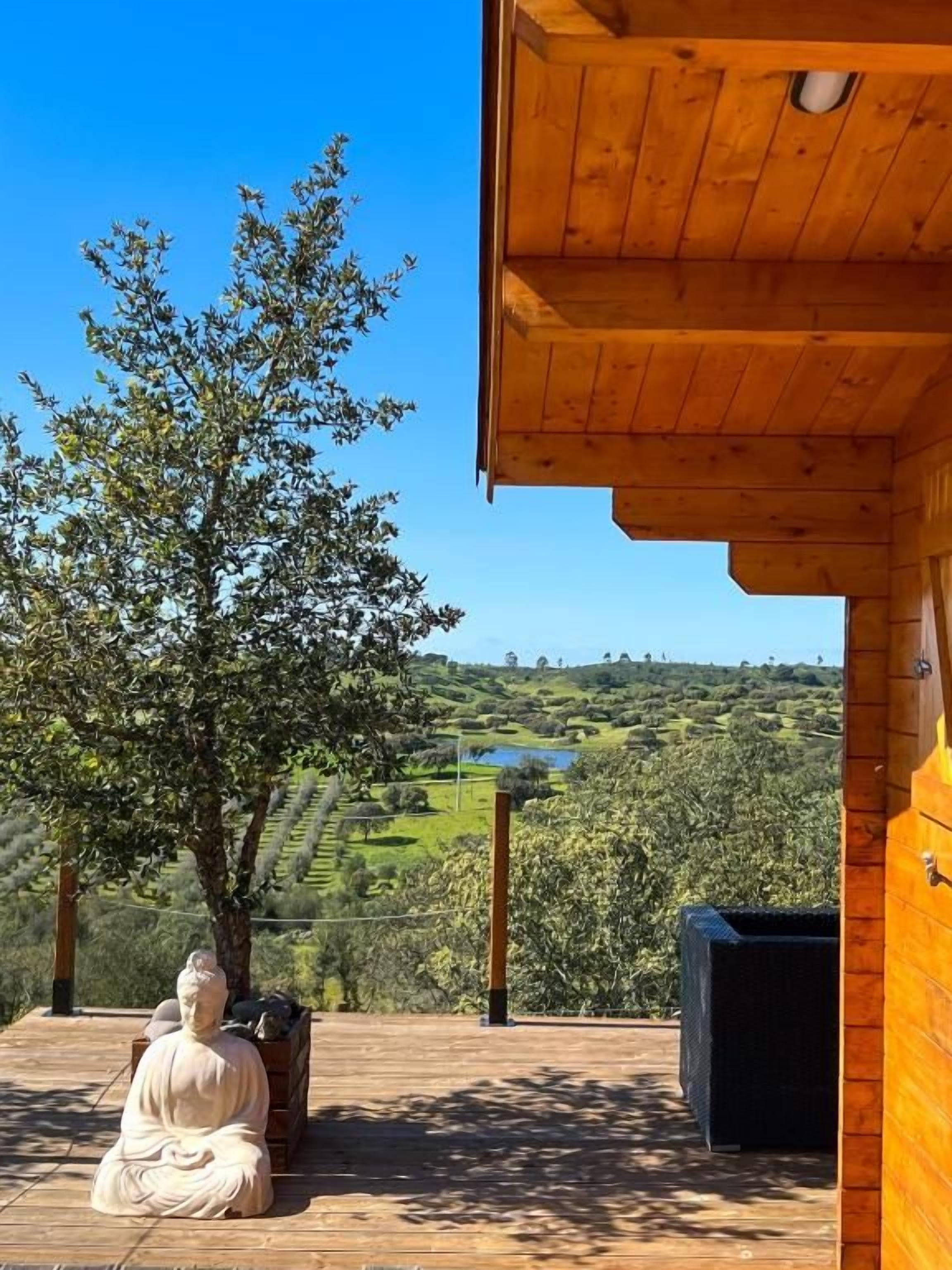 A wooden deck with a statue, overlooking a hilly landscape with a clear sky.