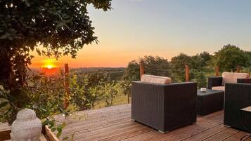 A wooden deck with outdoor furniture, a Buddha statue, and a sunset view.