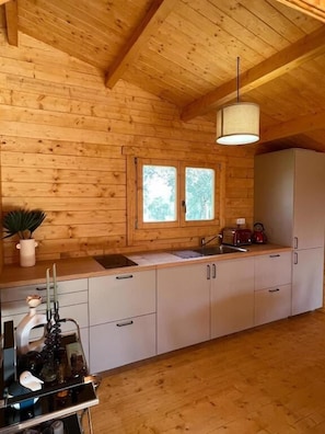 A wooden cabin interior with a kitchen area featuring a sink, cabinets, and a window.