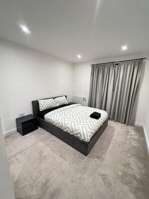 A modern bedroom with a bed, bedside tables, and a radiator. - Cedrus Place - 1 Bedroom (Southall)