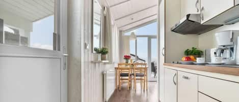 A modern kitchen with white cabinetry, a wooden dining table, and a view through the open door.