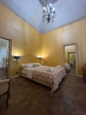 A hotel room with a bed, two wall-mounted lamps, a chandelier, and a mirror. - antico suites roma (Roma)