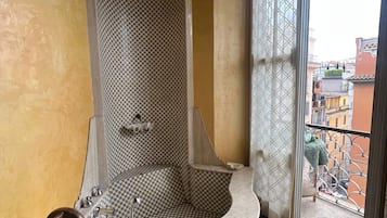 A bathroom with a checkered wall, a freestanding bathtub, and a view of the city through a window.