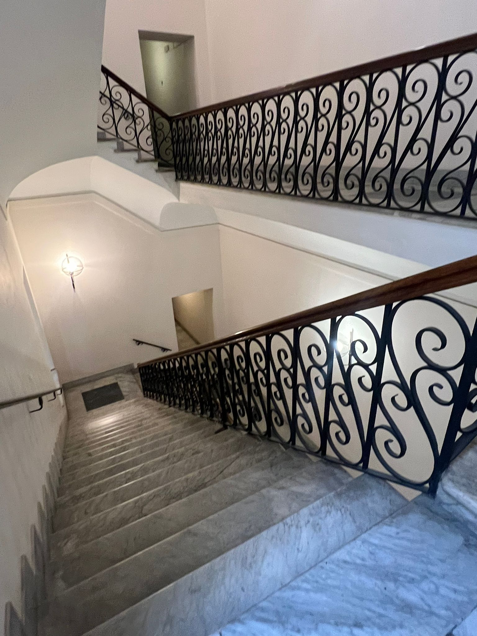 Una escalera con barandilla de hierro forjado negro y una lámpara en la pared.