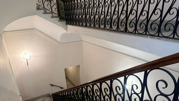Uma escadaria com corrimão em ferro negro e um acessório de iluminação na parede.