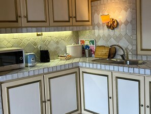 A kitchen with white cabinets, a microwave, a toaster, a bread box, and a wall-mounted light fixture. - antico suites roma (Roma)