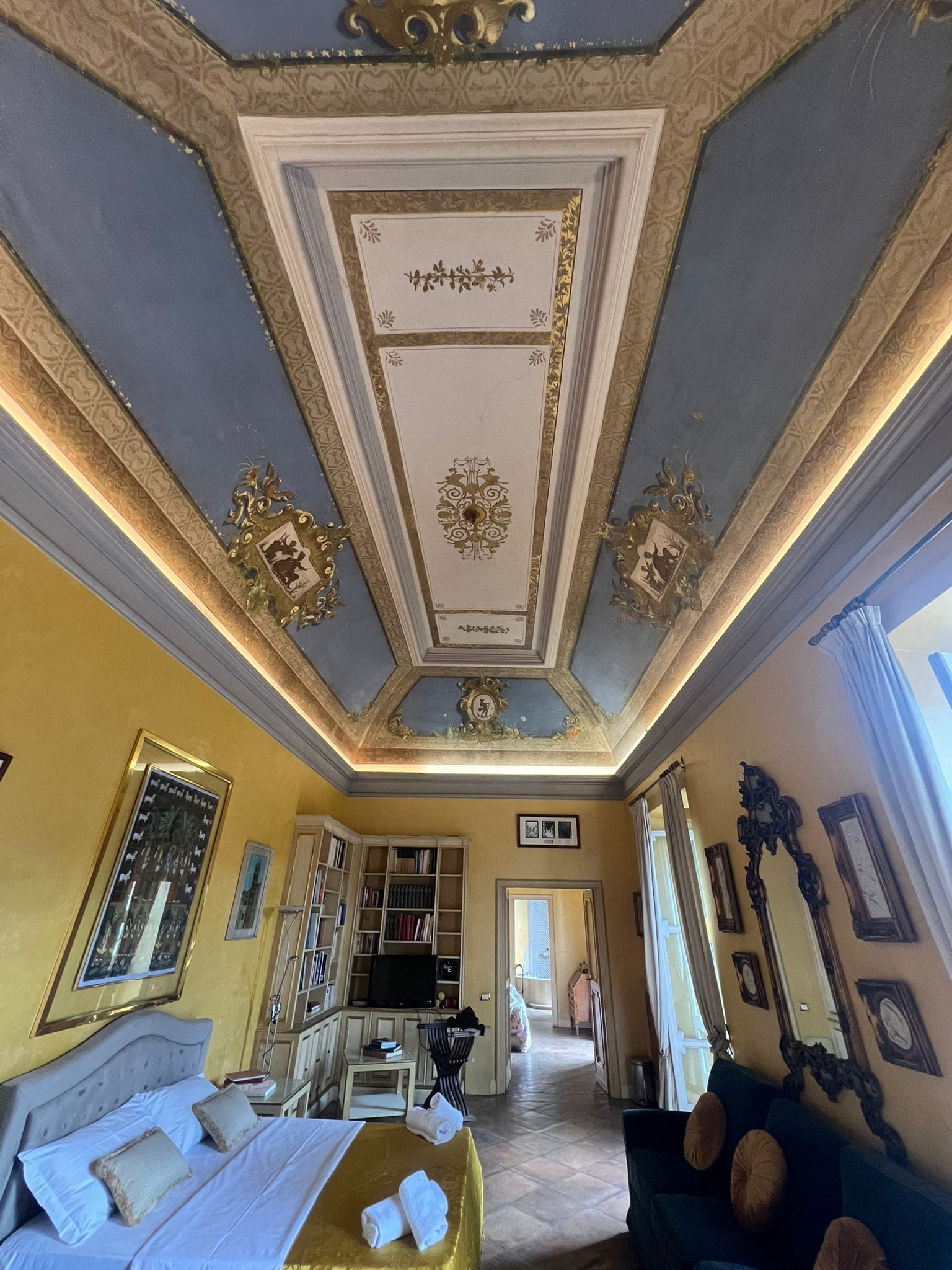 Una habitación de hotel con una cama, televisión, estantería y zona de comedor.