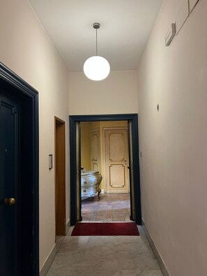 Um corredor com piso de mármore, tapete vermelho, luminária no teto e uma porta que dá para um aposento com porta de madeira e um armário.