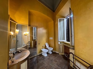 Casa de banho com lavatório, duas sanitas, espelho e janela.