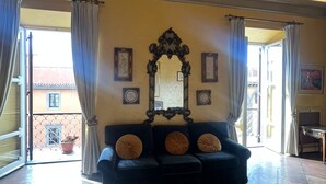 Quarto de hotel com uma cama grande, um sofá escuro, um espelho decorativo e uma varanda com vista.