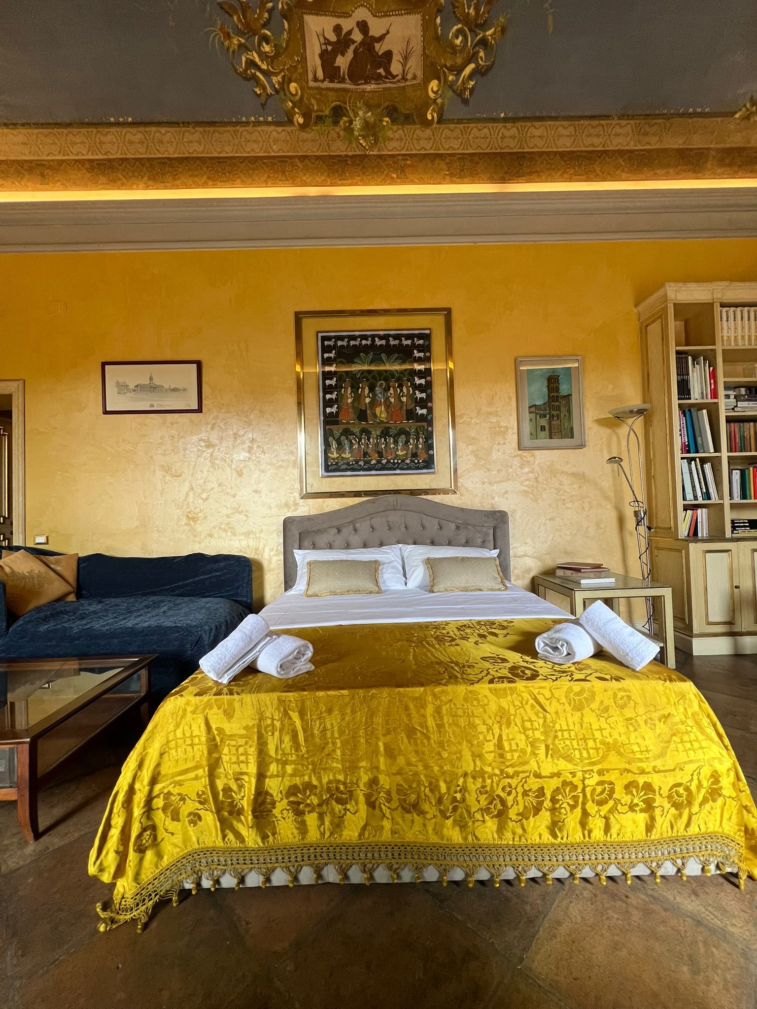 A room with a bed, a sofa, a bookshelf, and a framed picture on the wall.