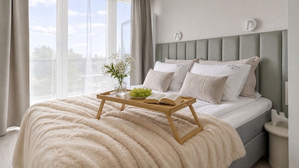 A bedroom with a bed, bedside tables, a window with curtains, and a bedside table with a tray holding a book and a vase with flowers. - Portovo Gdansk City Vibes Suites (Gdańsk)