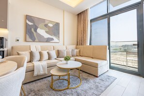 Ein modernes Wohnzimmer mit einem beigefarbenen Ecksofa, einem runden Couchtisch und einem großen Fenster mit Blick auf den Strand.