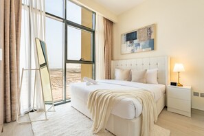 A hotel room with a large bed, a bedside table with a lamp, a painting on the wall, and a view through the window. - Cozy 1BR Near,Conveniently Located Just 15Min. fr. Downtown’s Iconic Attractions (Dubai)