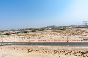 A desert landscape with a road, sparse vegetation, and distant buildings. - Cozy 1BR Near,Conveniently Located Just 15Min. fr. Downtown’s Iconic Attractions (Dubai)