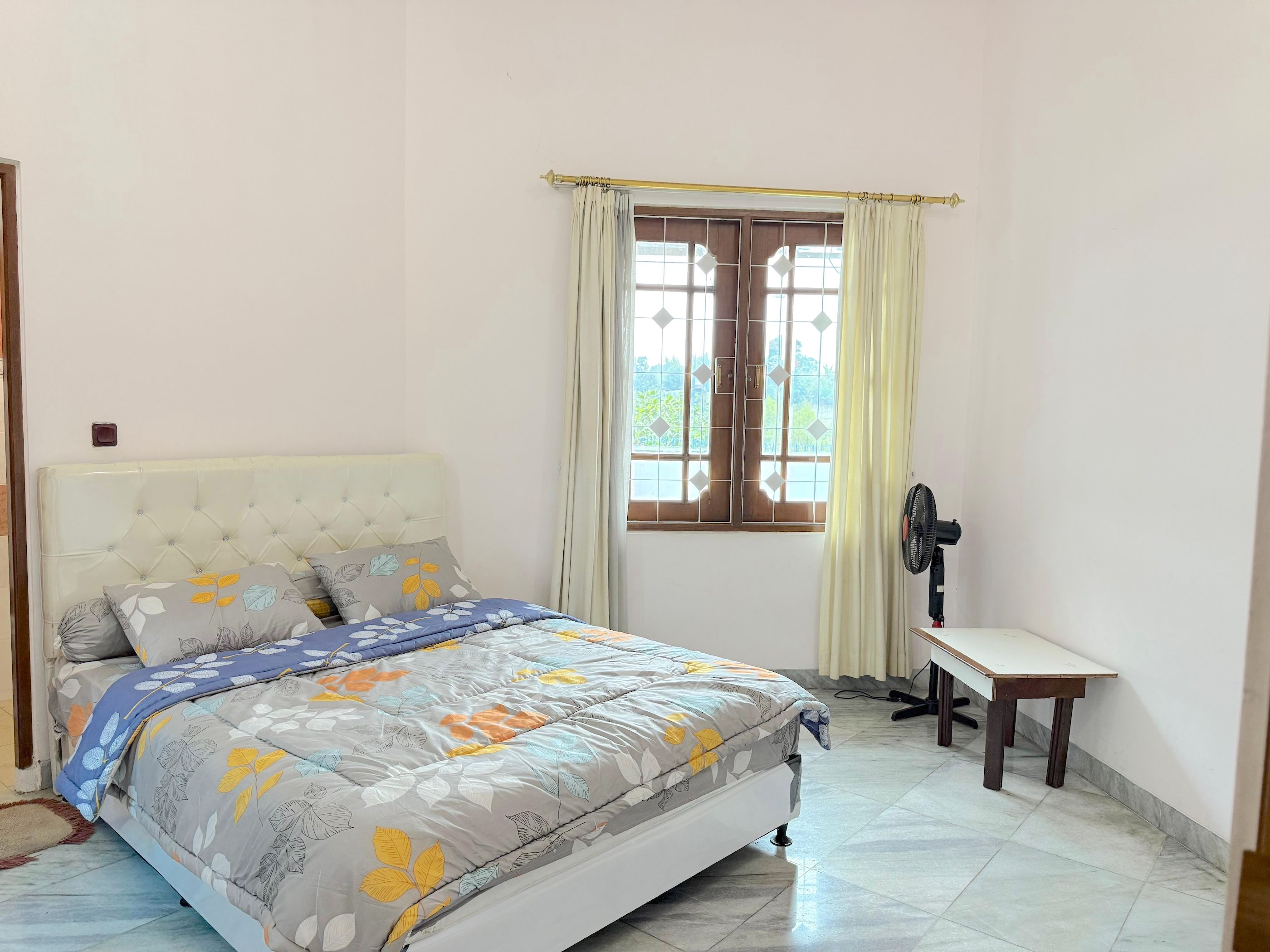 Une chambre à coucher avec un lit, une fenêtre avec des rideaux, un bureau et un ventilateur.