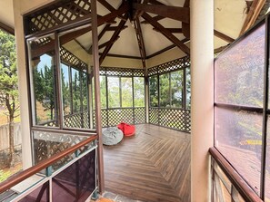 Un espacio exterior techado con suelo de madera, un cojín rojo y un panel de celosía.