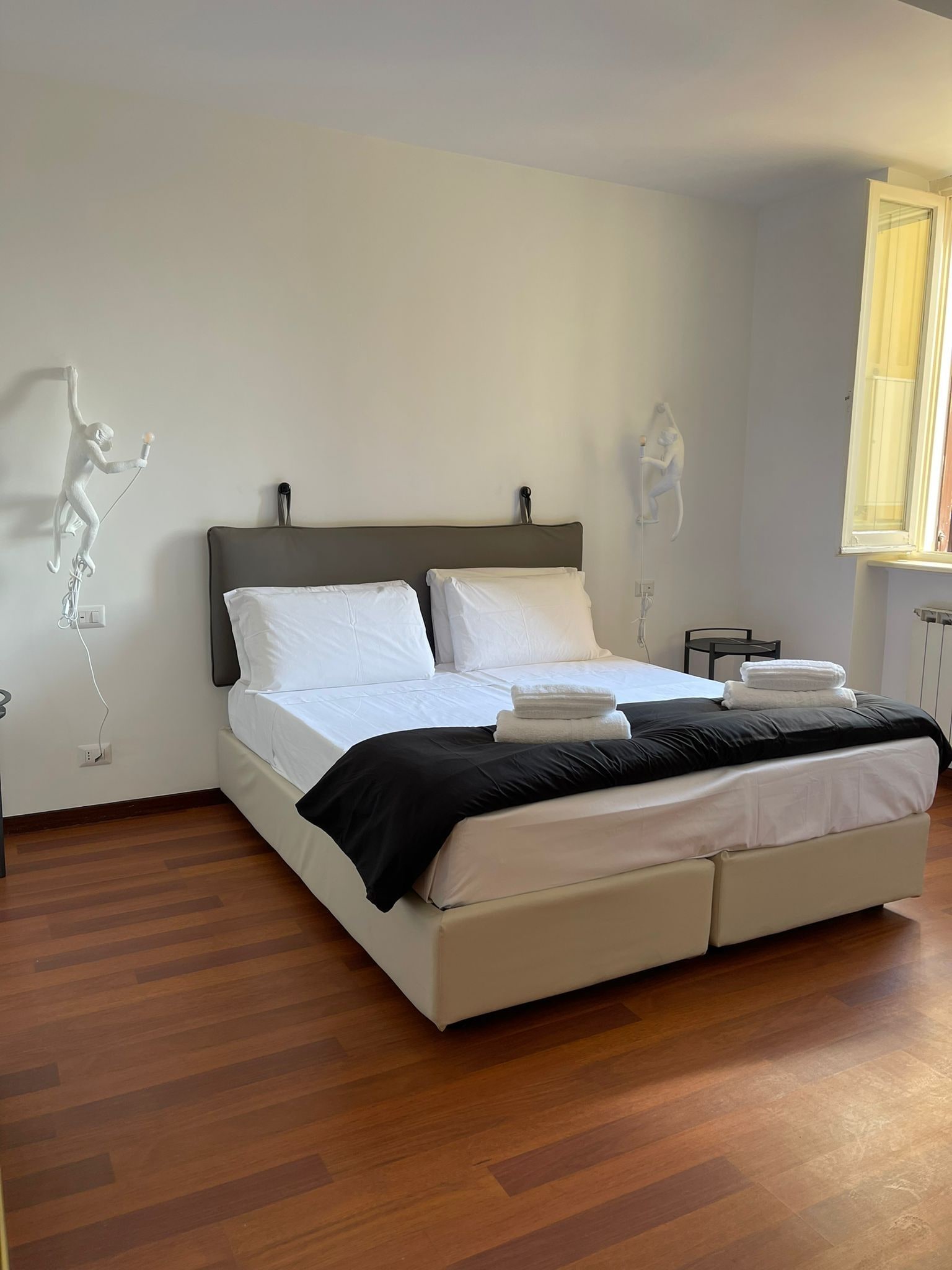 A modern bedroom with a bed, white linens, a black throw, and a wooden floor.