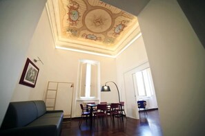 A room with a dining table, chairs, a sofa, and a ceiling with intricate designs. - Luciano Monti Apartment (Roma)