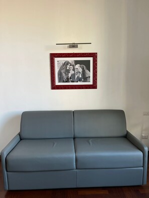 A grey sofa in a room with a framed black and white photograph on the wall. - Luciano Monti Apartment (Roma)