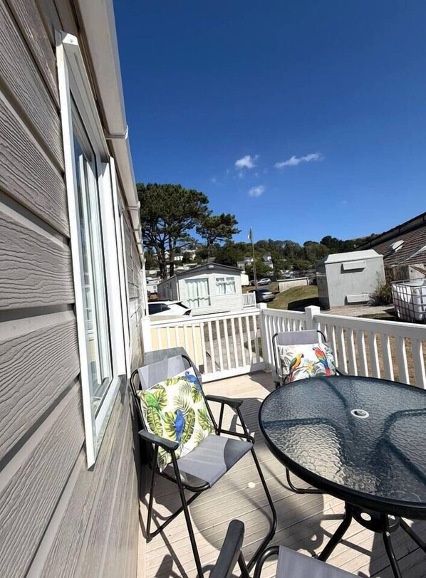 A patio with a round table and two chairs, a white railing, and a view of neighboring houses.