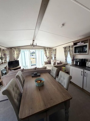 A compact living space with a dining table, sofa, television, and kitchenette.