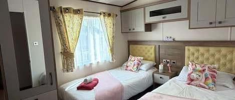 A hotel room with two beds, a wardrobe, a mirror, and a television.
