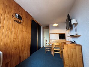 Ein kleiner Raum mit Holzboden, einem Schreibtisch mit Stühlen, einem Fernseher und einer Lampe.