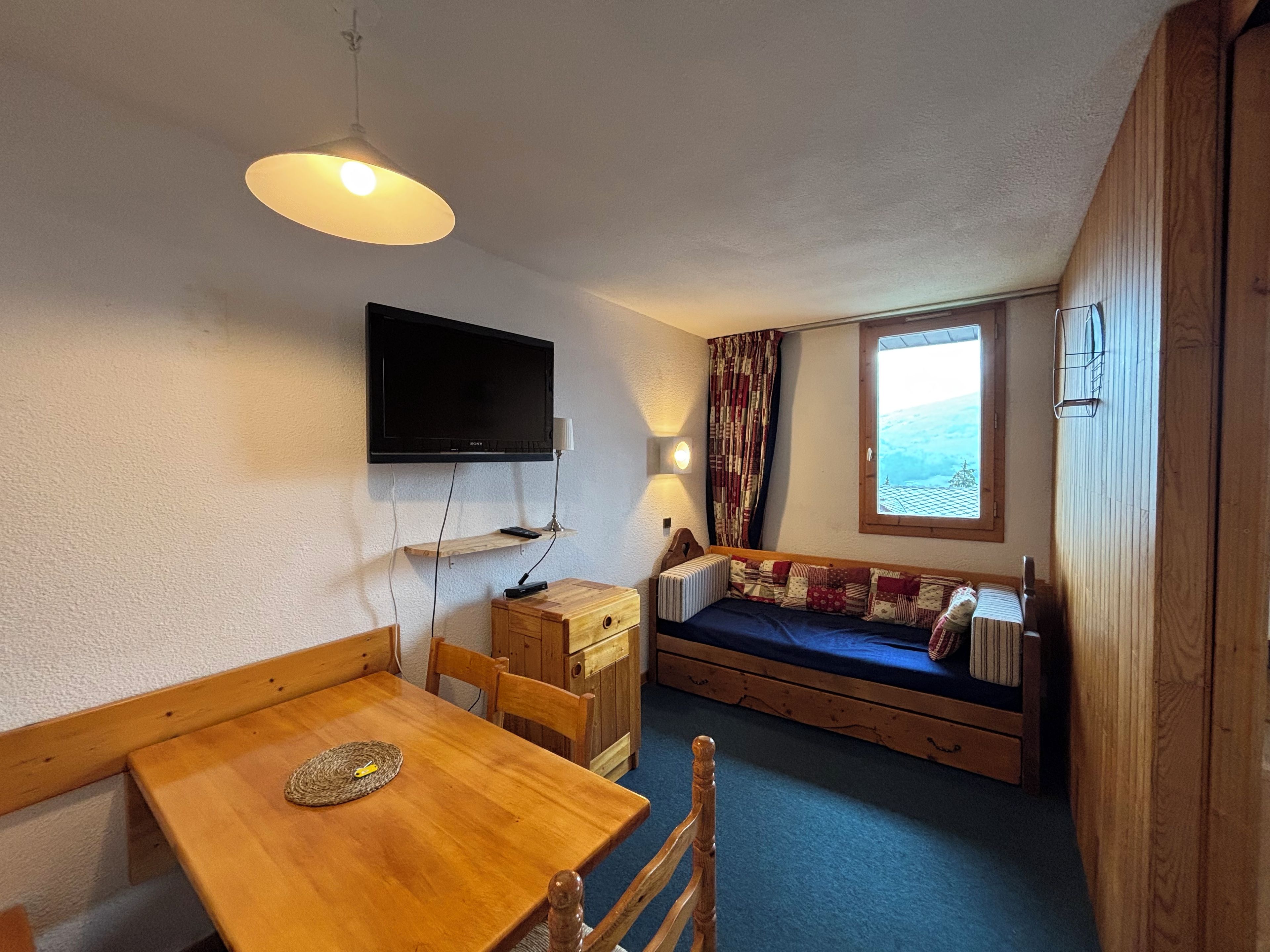 Ein gemütlicher Raum mit Holztisch, einer Couch, einem Wand-Fernseher und einem Fenster mit Blick.