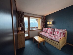 A cozy room with a wooden bench, a sofa with patterned cushions, a small table, and a window offering a view of mountains. - Apartment in Les Coches (La Plagne-Paradiski) - Right on the slopes (La Plagne Tarentaise)